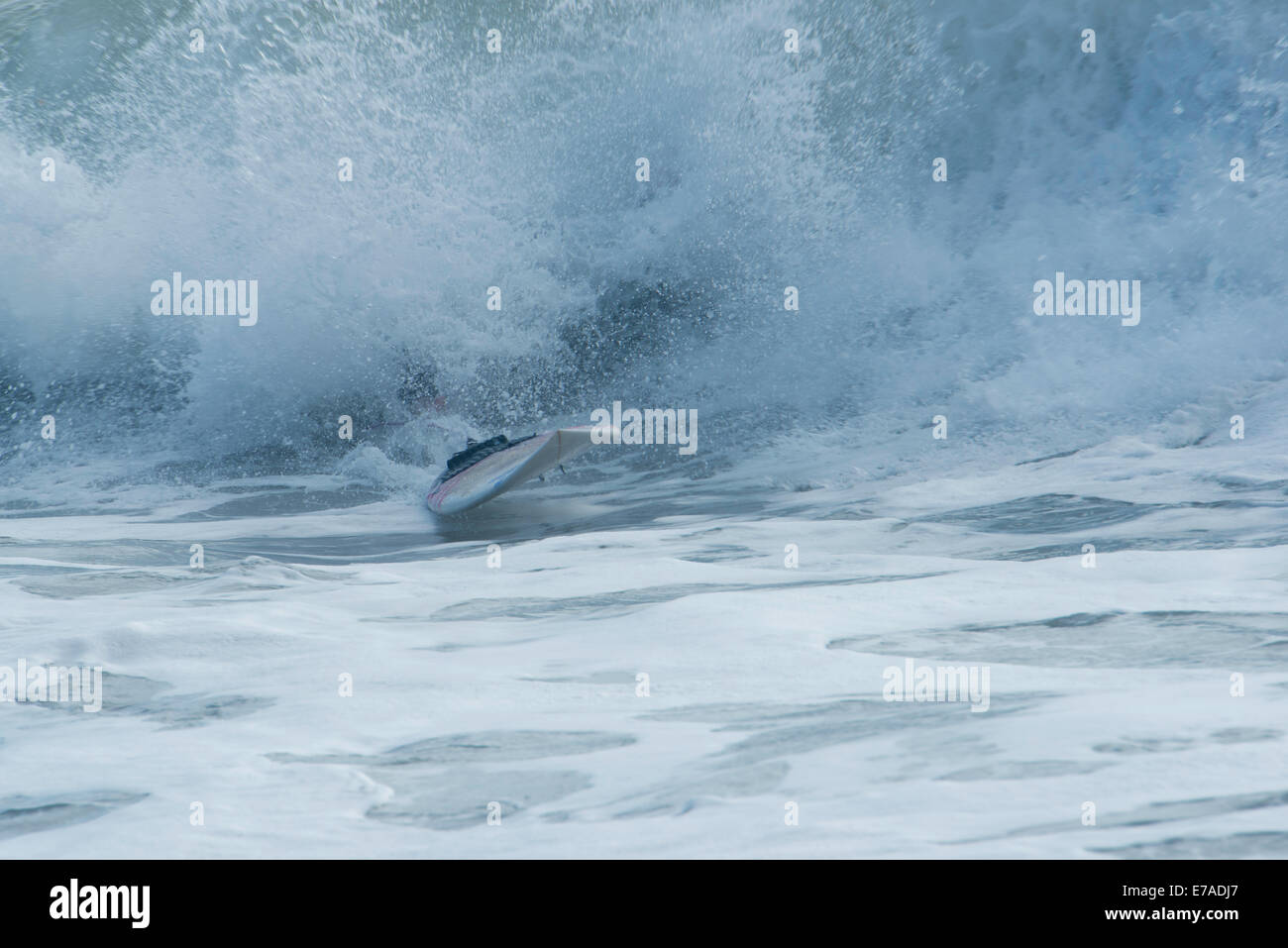 Surfboard appearing from waves after surfer has wiped out Stock Photo
