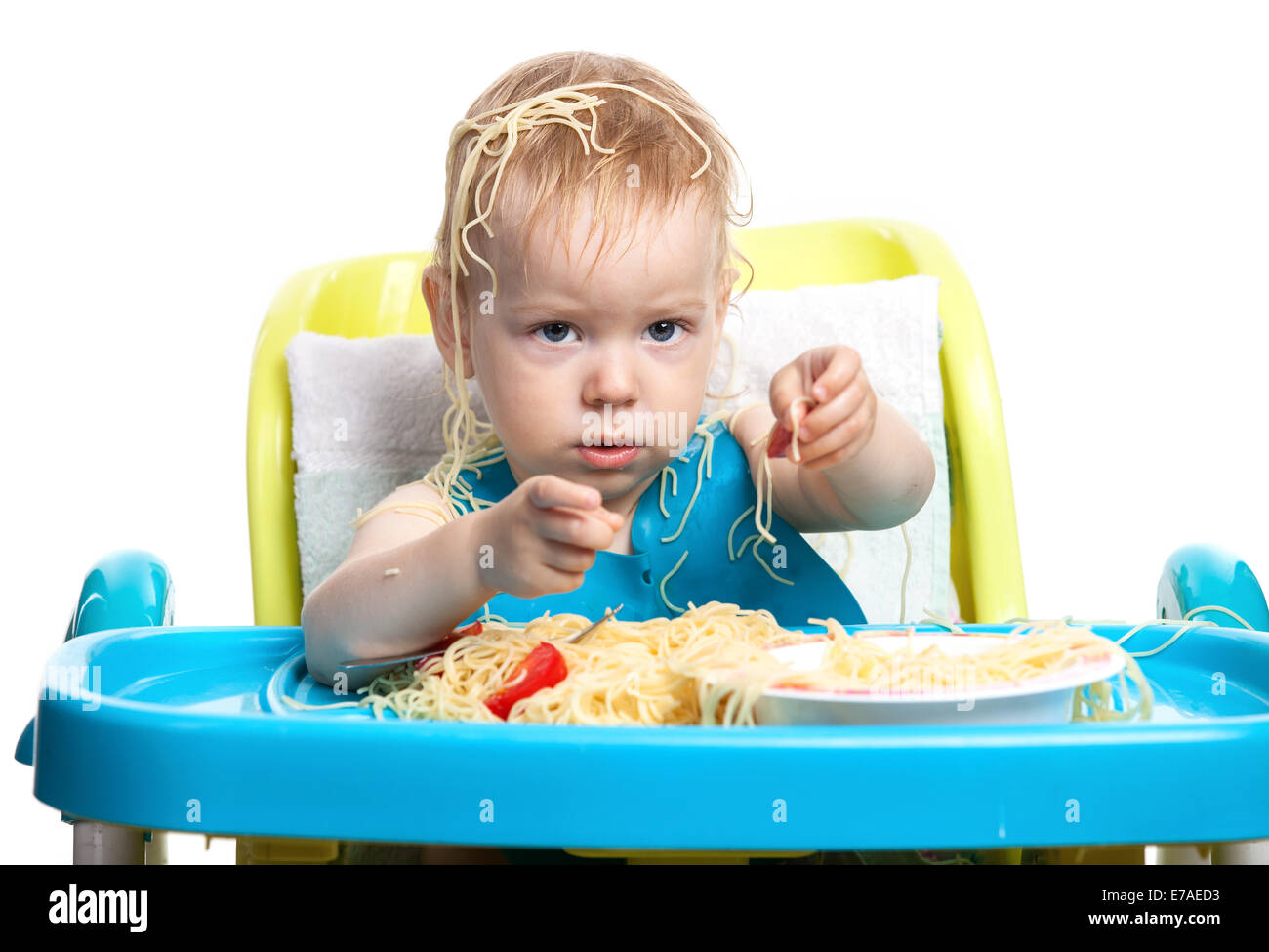 Little blond boy eating spaghetti, with pasta on his head Stock Photo