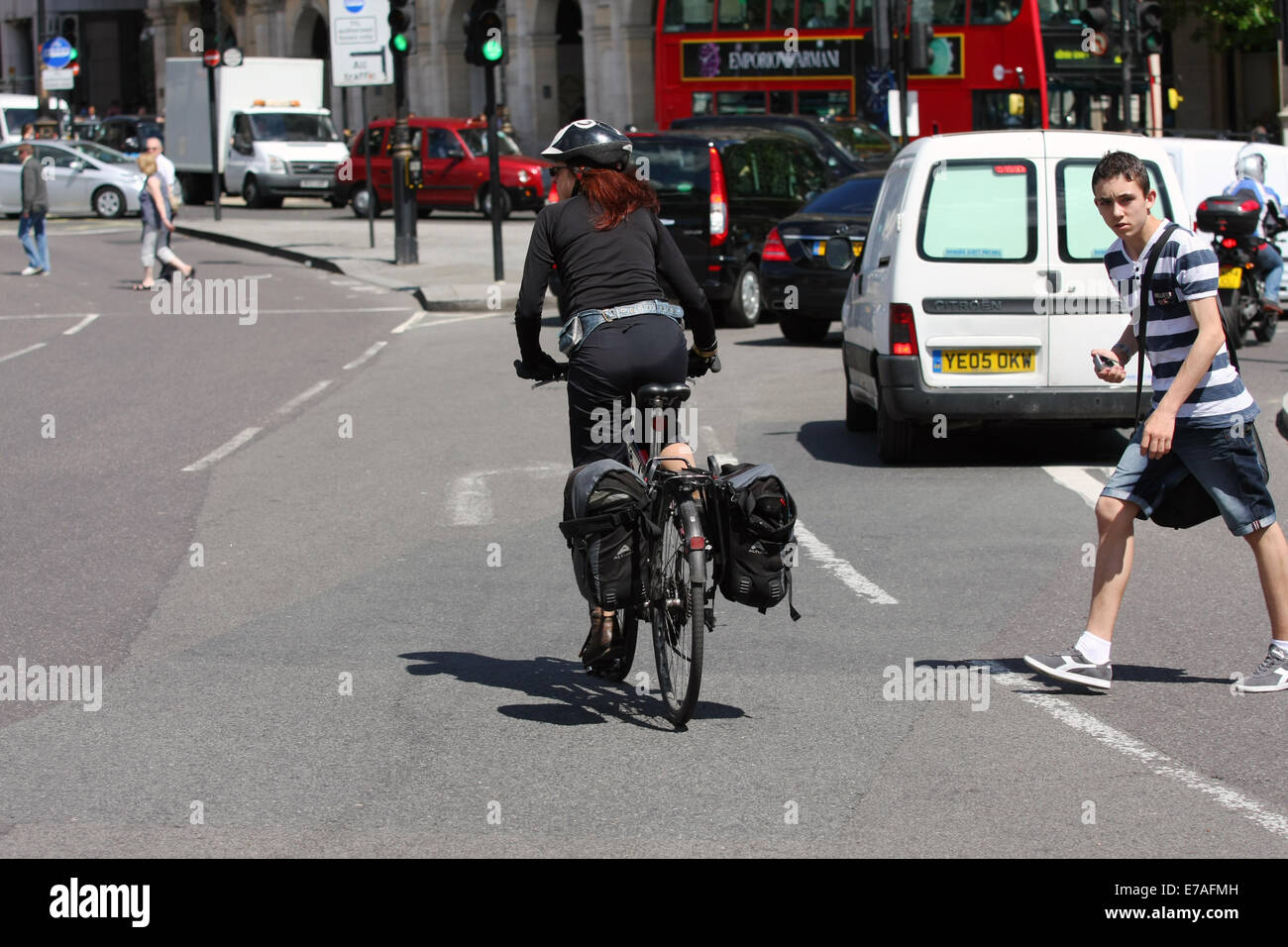 A female cyclist riding along a London road and a pedestrian crossing the road just after the cyclist has passed. Stock Photo