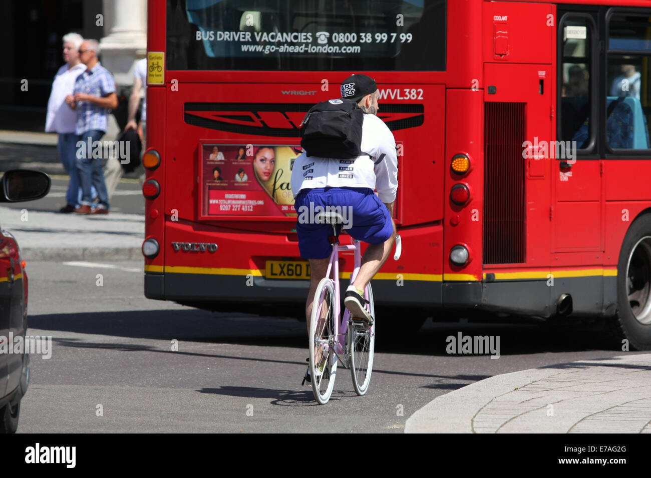 A cyclist traveling around a roundabout, behind a red London bus Stock ...
