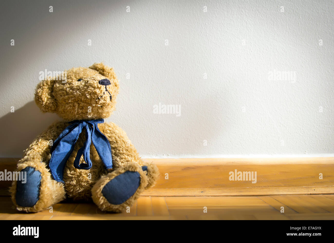 teddy bear sitting against grey wall Stock Photo