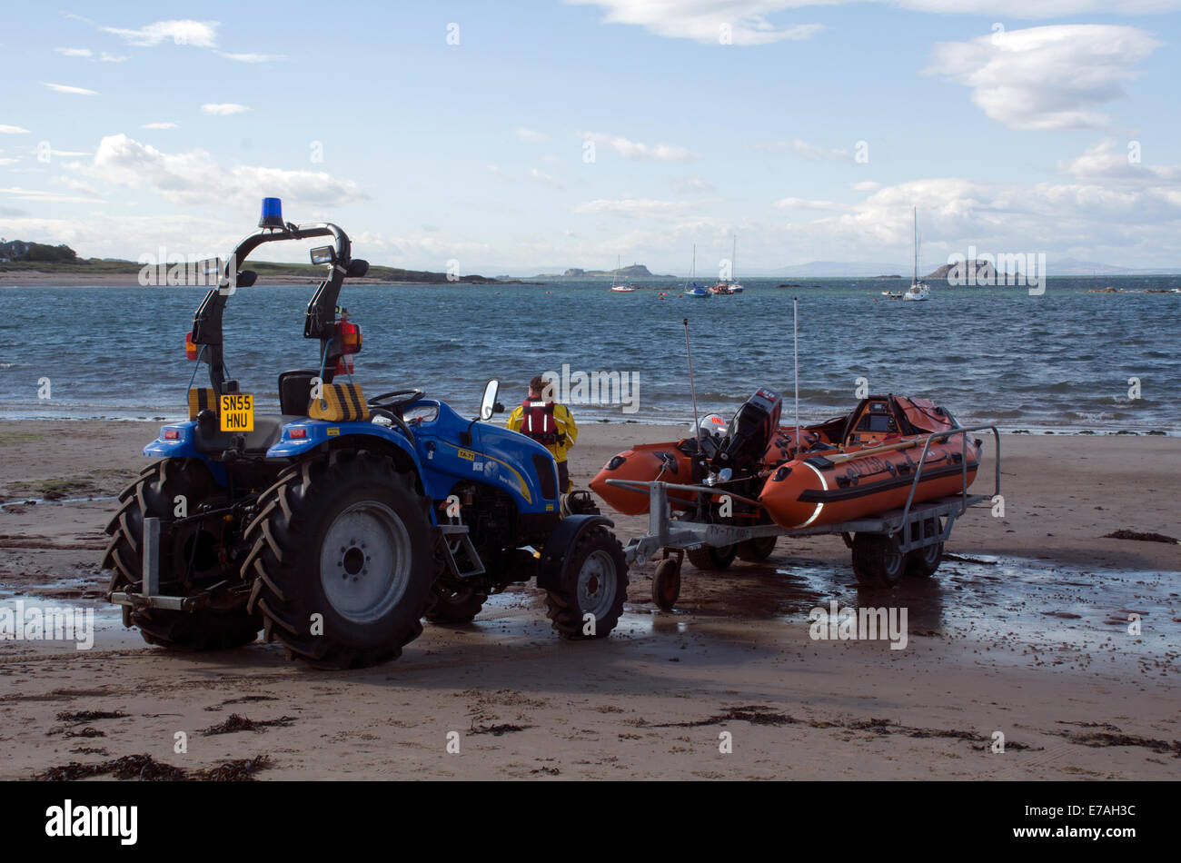 An RNLI volunteer waits by the tractor that pulls boat trailers and an RNLI inflatable boat ready to launch at North Berwick. Stock Photo