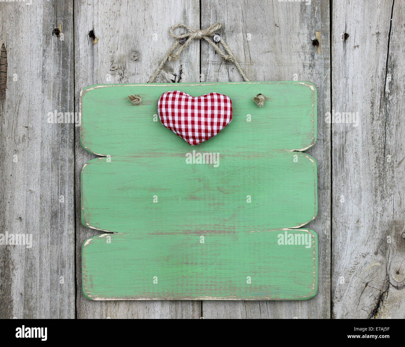 Red checkered heart on blank green sign hanging on old weathered wood door Stock Photo