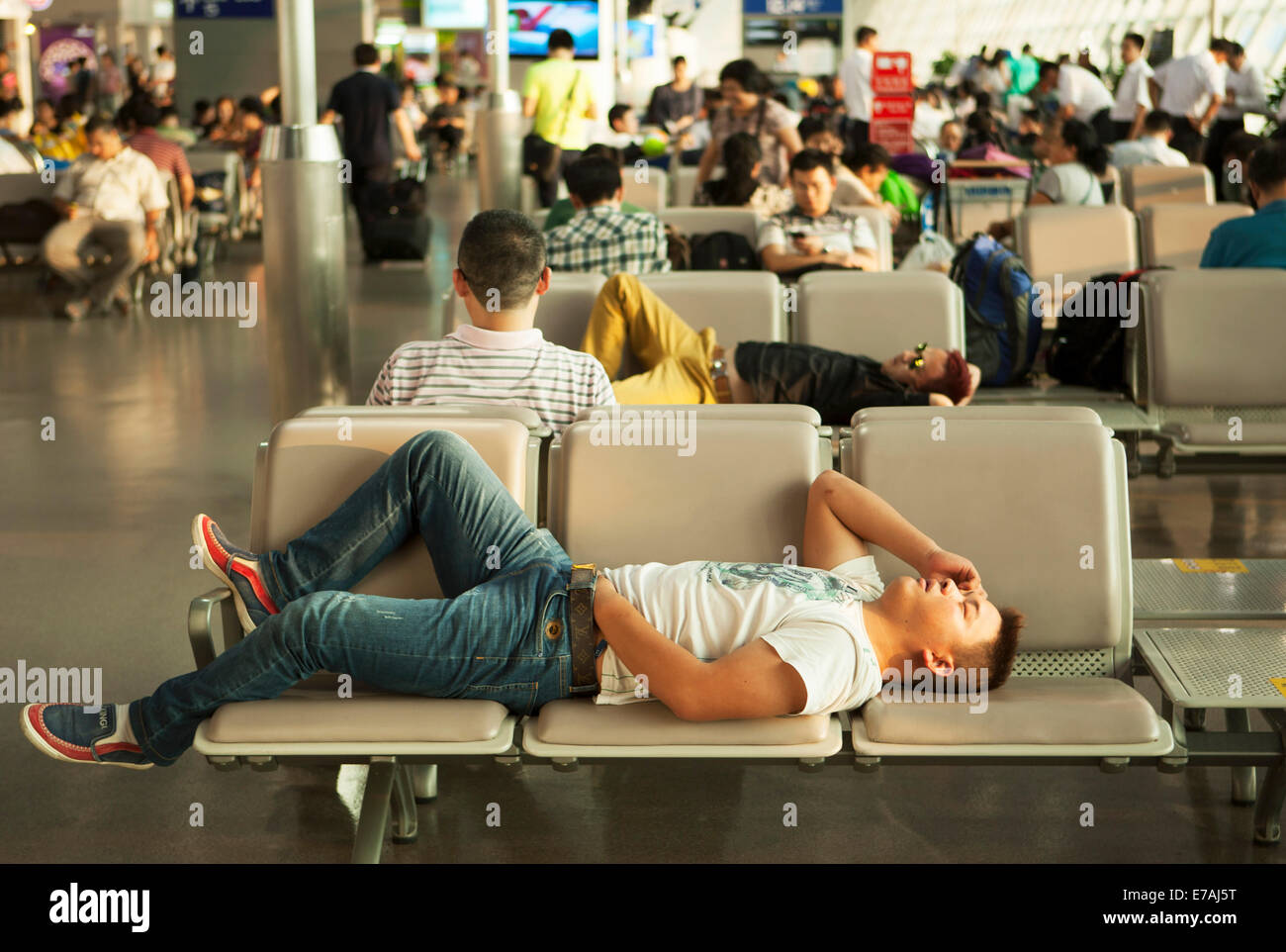 Chinese international Airport, China. Air passengers waiting resting sleeping napping in departure lounge chairs seats Stock Photo