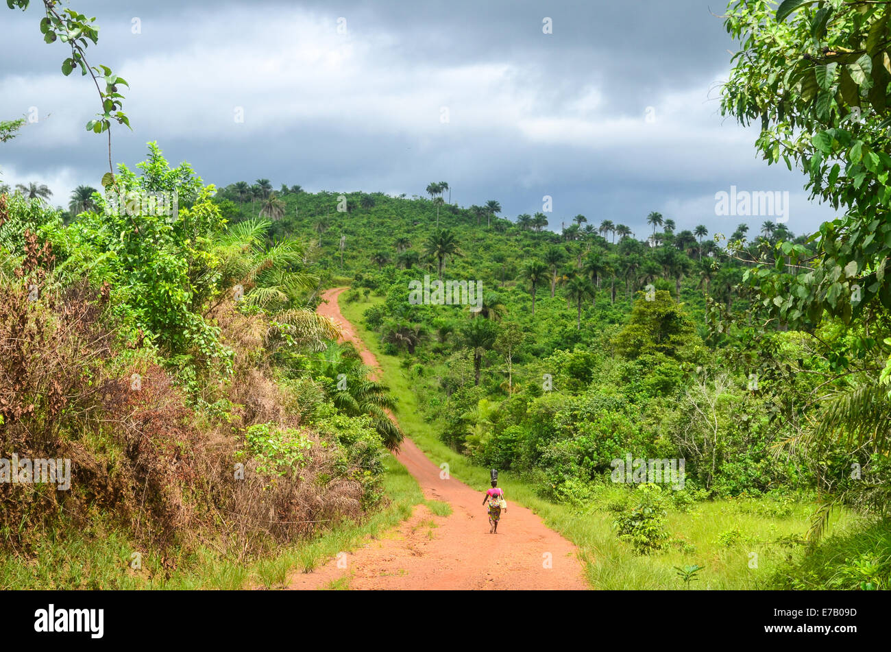 A woman carrying a bucket on her head and a child in her back on the red earth dirt roads of the east of Sierra Leone Stock Photo