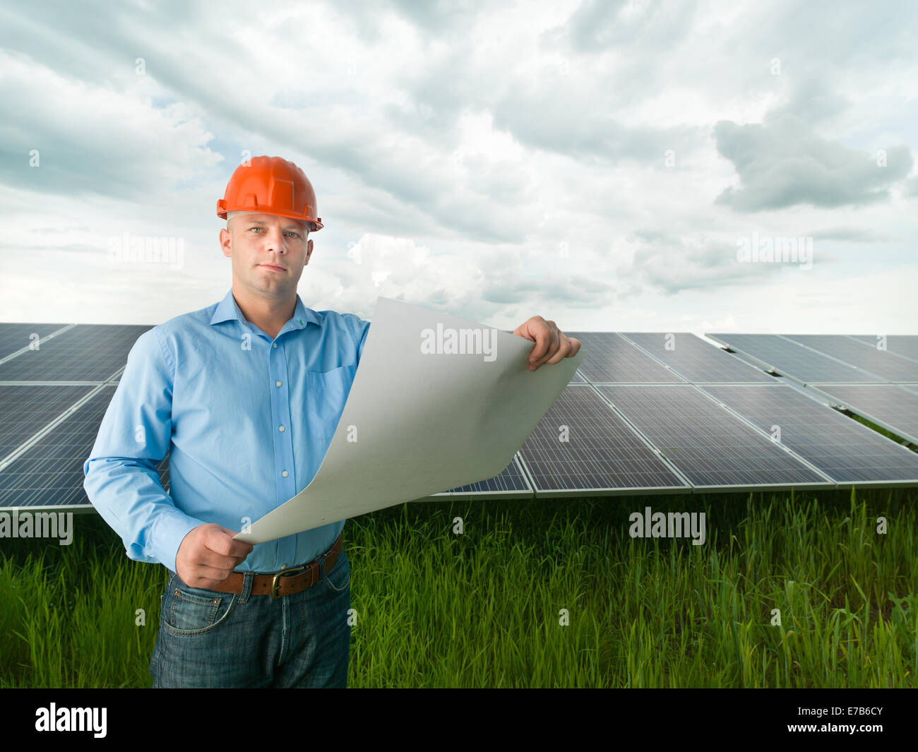 male engineer standing in solar panel station, holding blueprints Stock Photo