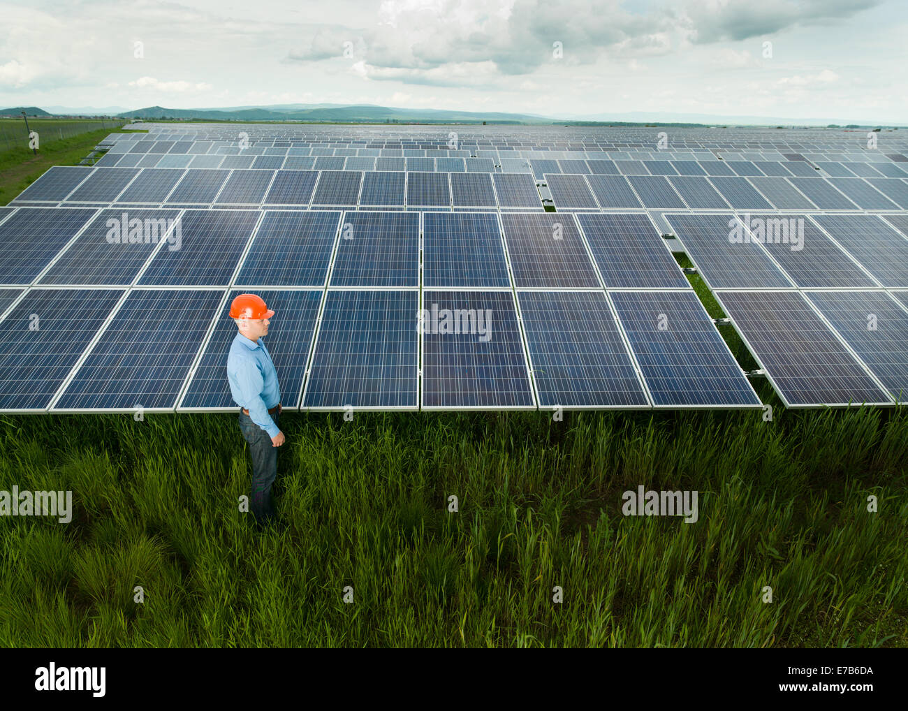 man dressed in engineer clothes and equipment standing near solar panels, outdoors, with clouded sky Stock Photo