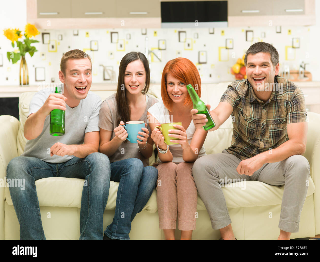 portrait of four young caucasian friends sitting on sofa holding drinks, watching a television show Stock Photo