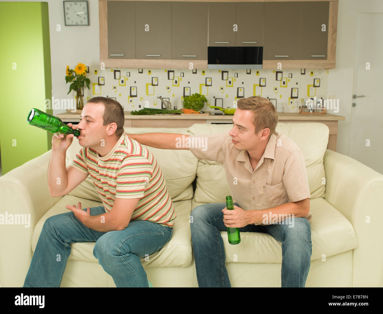 two young caucasian men sitting on couch, holding beer bottles, consolation Stock Photo