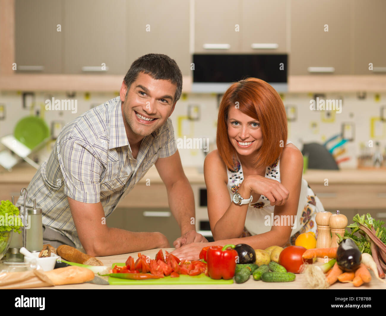 portrait of young happy couple standing in kitchen with fresh vegetables on table Stock Photo