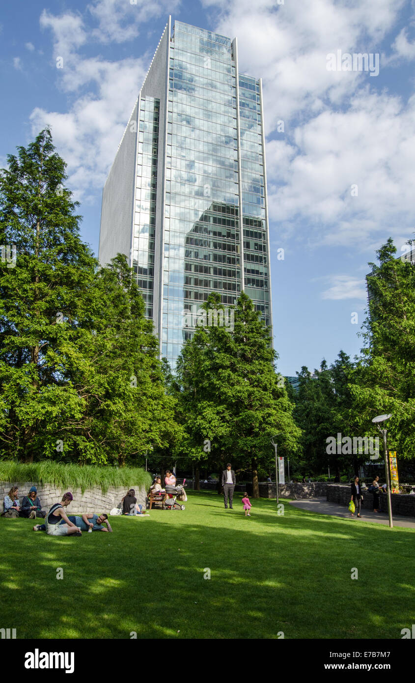 LONDON, UK  JULY 1, 2014:  Sunbathers in Jubilee Park overlooked by Clifford Chance headquarters, London Docklands. Stock Photo