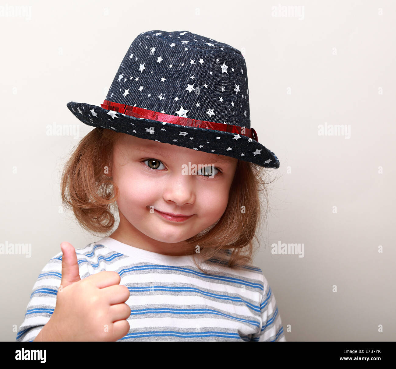 Cute kid girl in blue hat showing thumb up sign Stock Photo