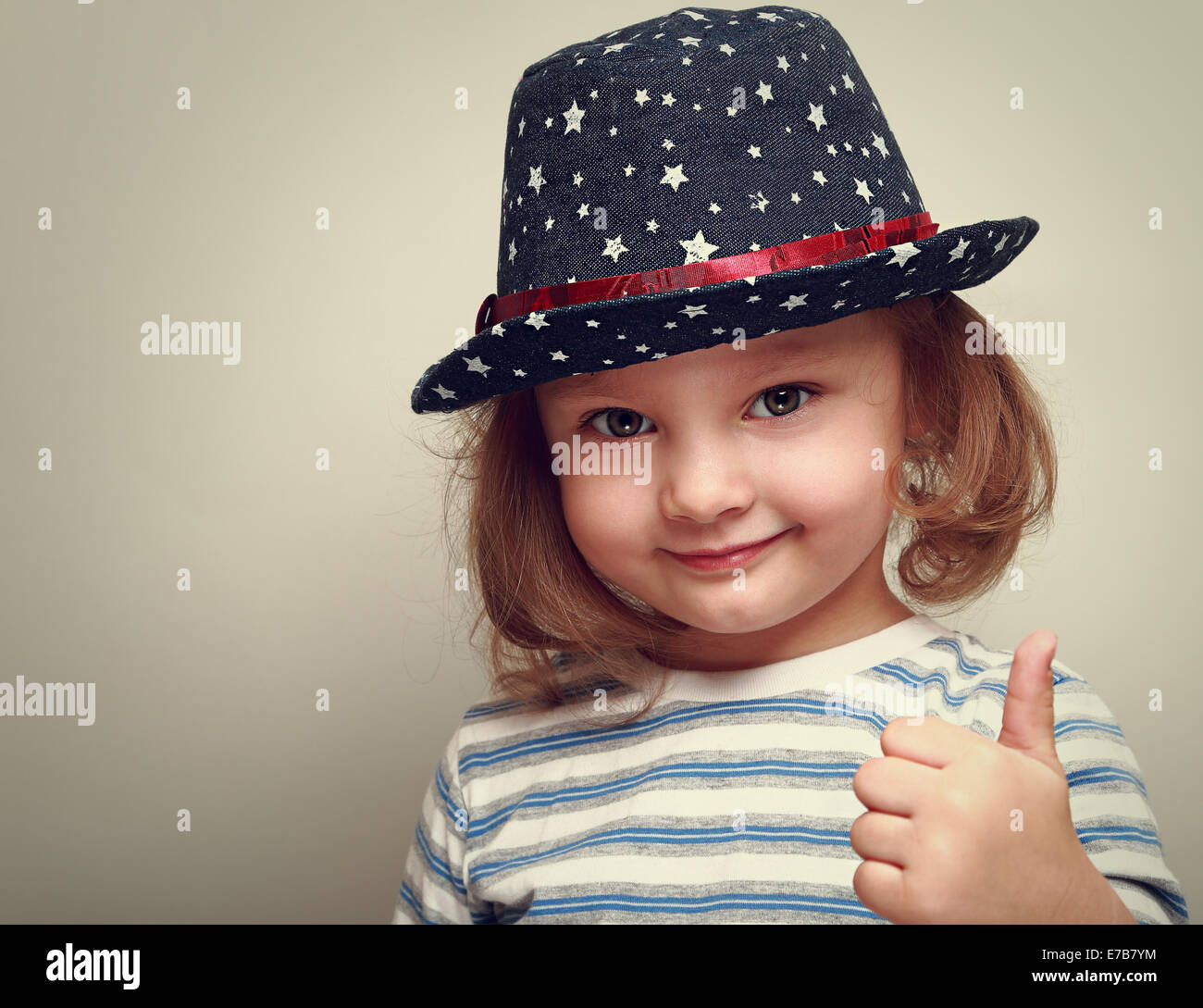 Smiling kid girl in blue hat showing thumb up sign. Closeup Stock Photo