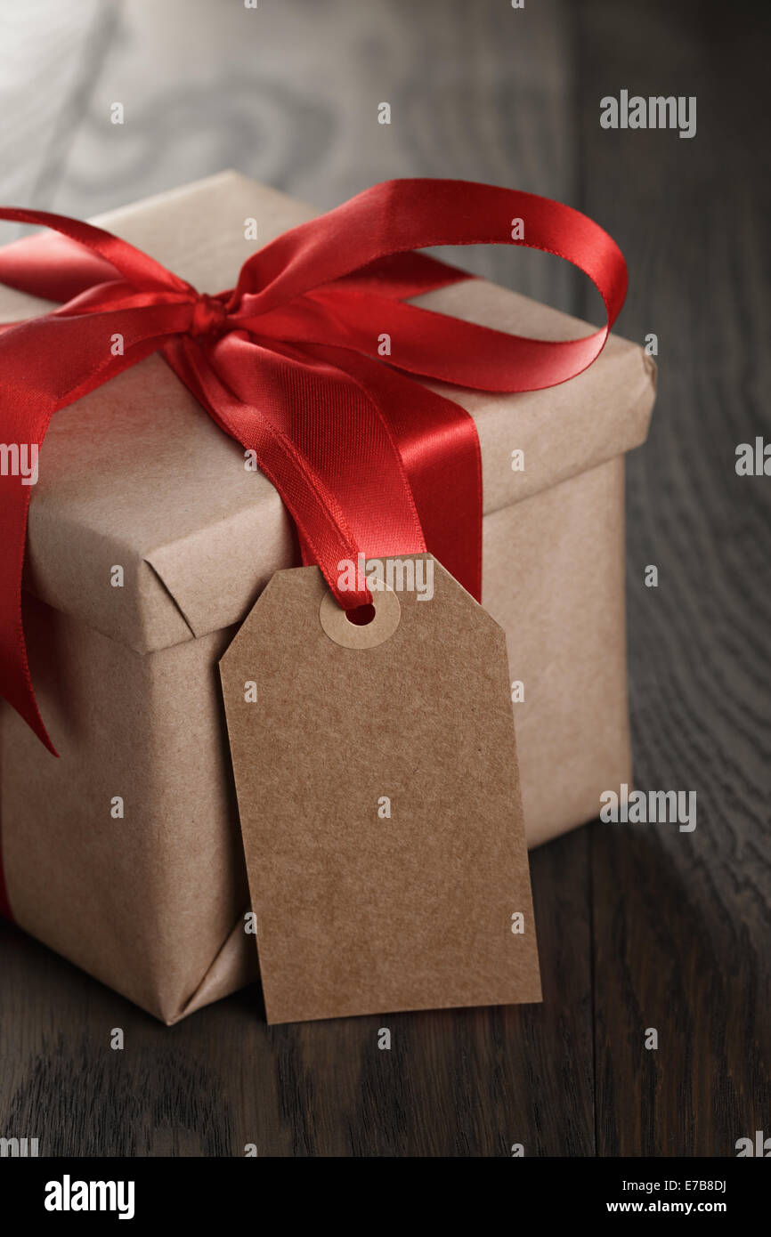 rustic gift box with red ribbon bow and empty tag, on old wood table ...