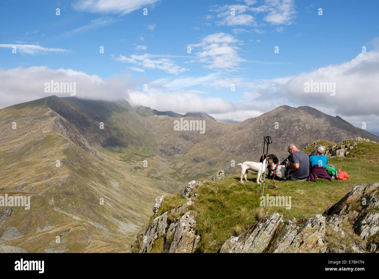 Hillwalkers resting on Yr Aran summit with view across Cwm Llan to cloud topped Snowdon peak in mountains of Snowdonia National Park North Wales UK Stock Photo