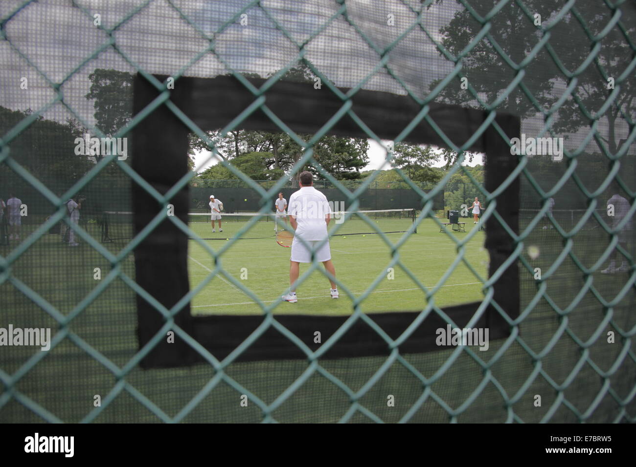 People playing tennis as seen through an opening in protective fencing,  USA, 2014, © Katharine Andriotis Stock Photo