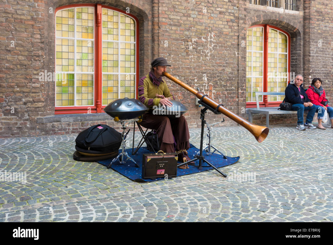 A street busker playing a steel drum and a didgeridoo  in the inner courtyard of the Market Hall in Bruges, Belgium Stock Photo