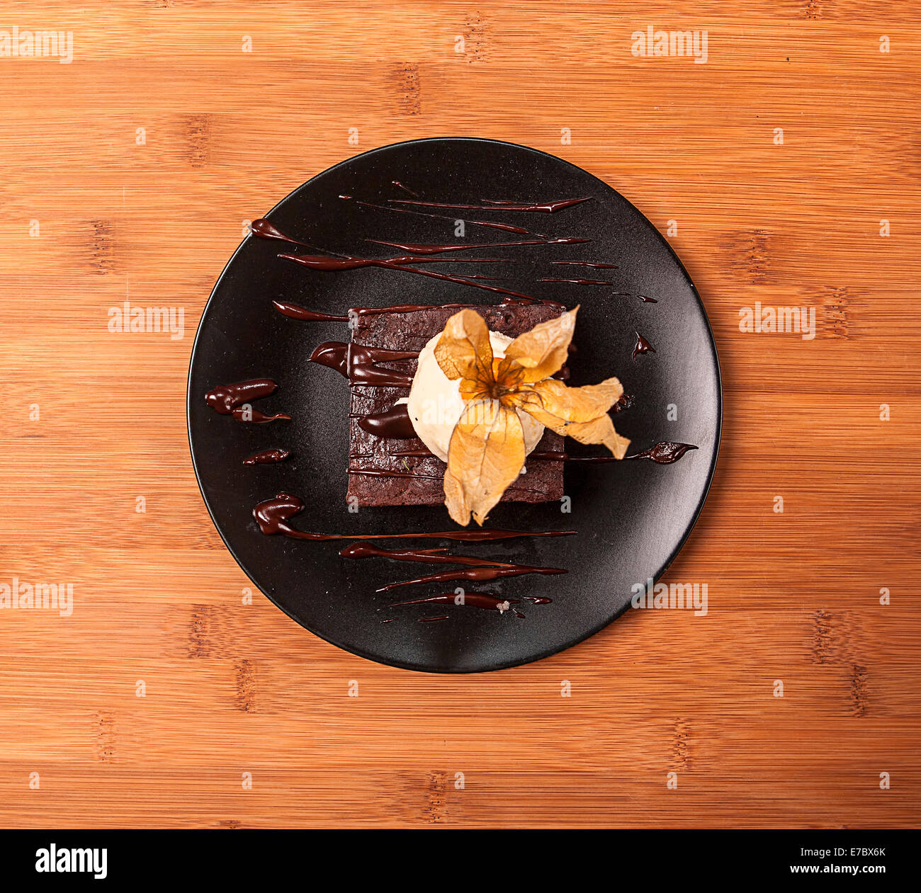 Brownie cake with chocolate and vanilla ice cream on a dark plate on a wooden table Stock Photo