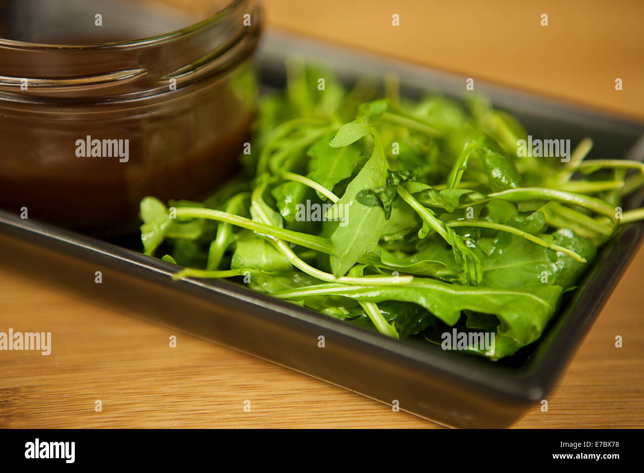 Rucola salad on a dark plate on wooden table with sauce Stock Photo