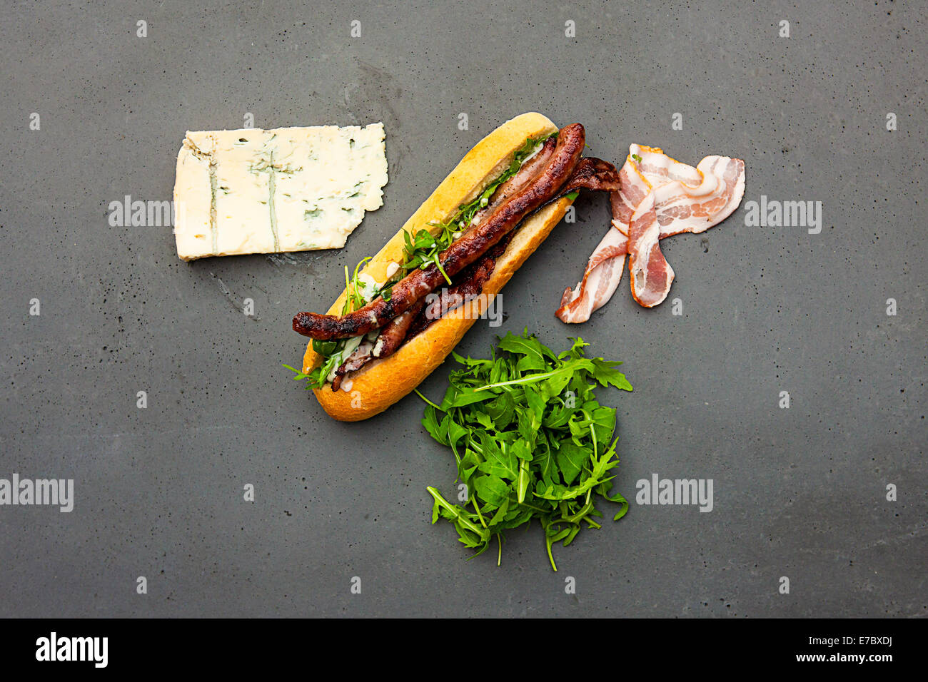 Modern hot dog with lamb sausage, bacon, rucola, gorgonzola sauce on concrete table Stock Photo