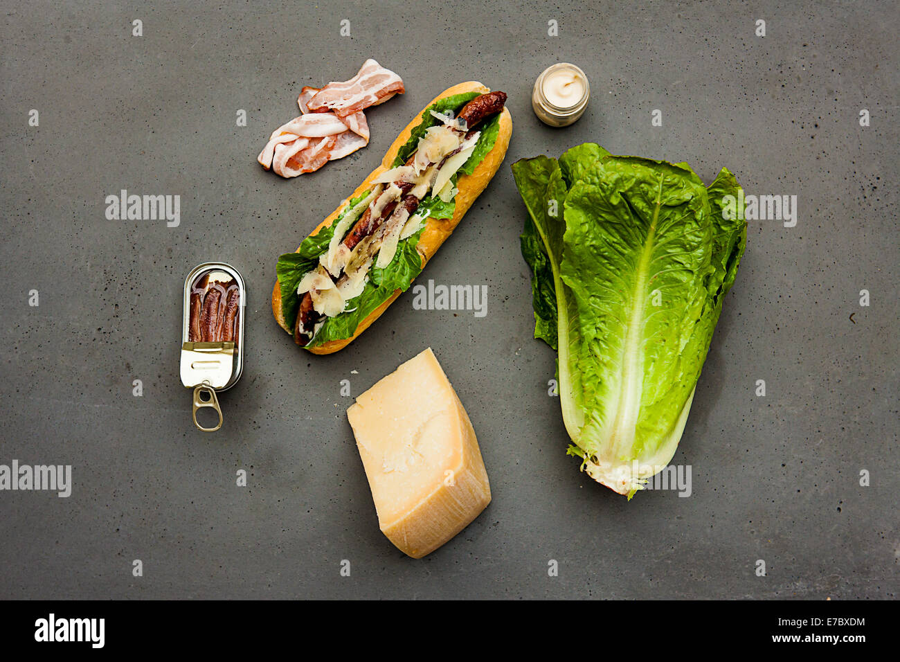 Modern hot dog with lamb sausage, bacon, parmesan, romaine lettuce, anchovies, dressing sauce on concrete table Stock Photo