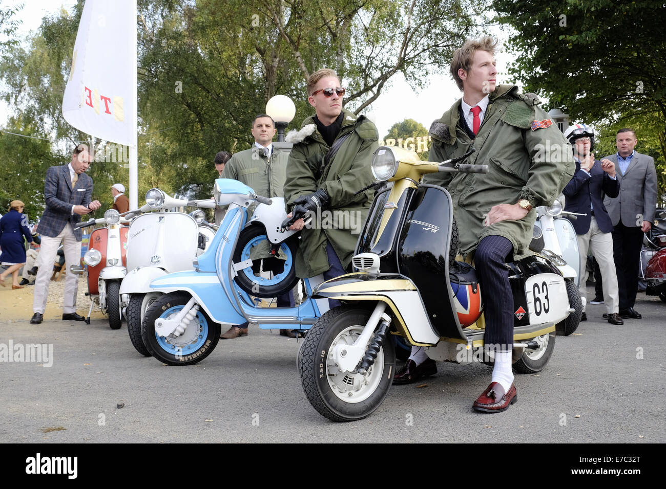 A group of young men twenties smartly dressed as mods and are wearing parkas staypress trousers and loafer shoes are sitting on italian styled lambretta and vespa motor scooters whilst attending the . 2014. Goodwood revival event at the goodwood motor circuit near chichester in west sussex uk,  The Goodwood revival offers some superb motor racing action on the circuit and entertainment for all of the family in the grounds, spectators are encouraged to dress in period and vintage clothing and become part of the event. Stock Photo