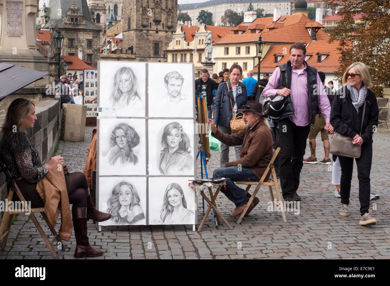 Street artist at work on Charles Bridge in Prague with passing tourists Stock Photo