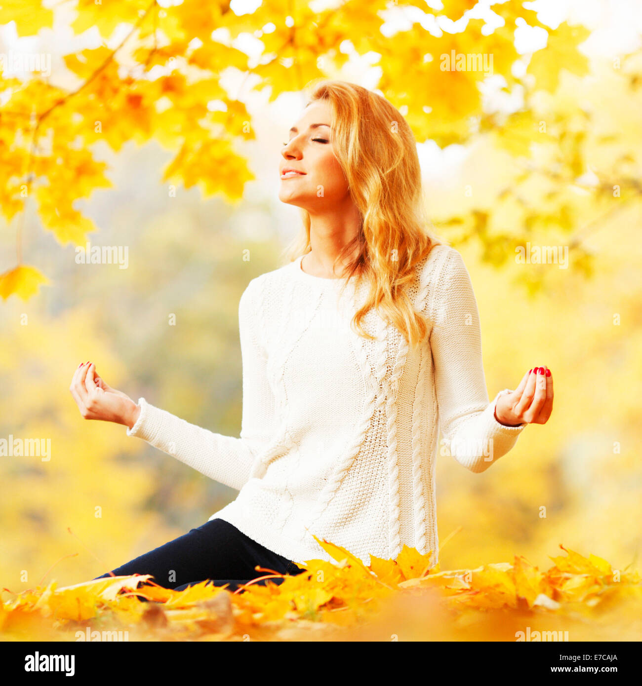 Beautiful young woman sitting in autumn park in lotus yoga position ...