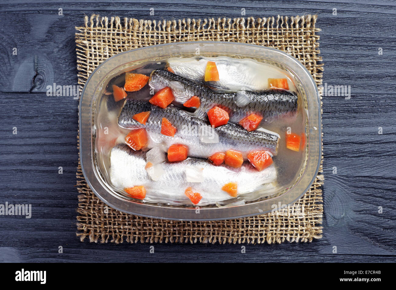 Marinated fish with carrots in jar on dark wooden background Stock