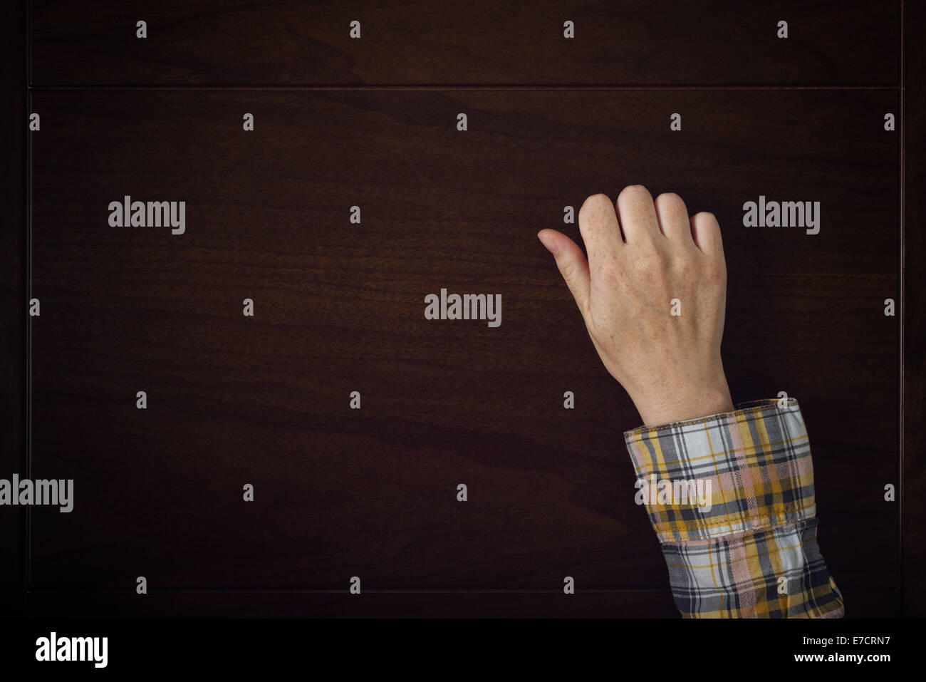 Female hand is knocking on wooden door, conceptual image. Visitor or guest is at the door. Stock Photo