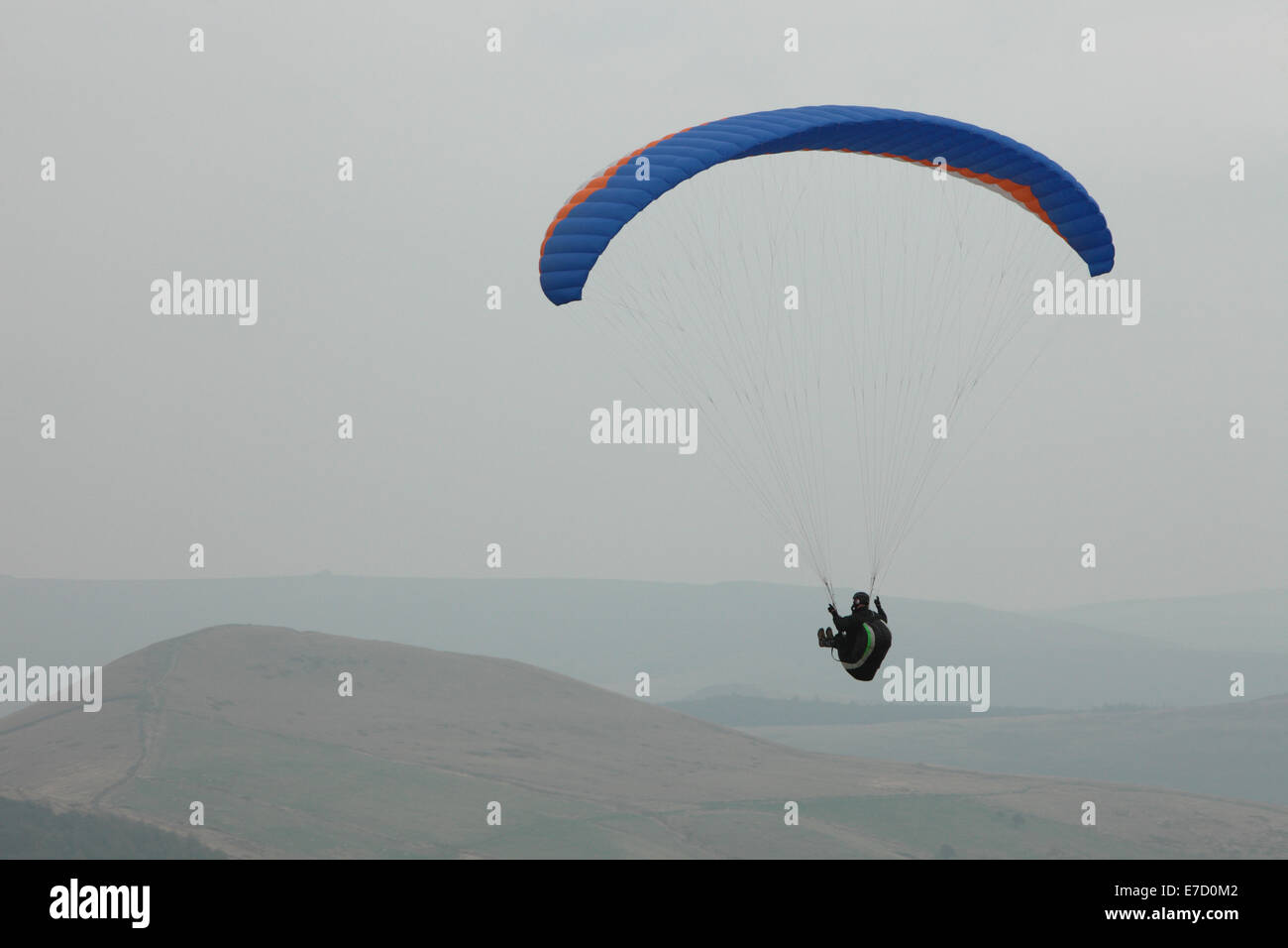A paraglider flies over the Derbyshire Peak District from right to