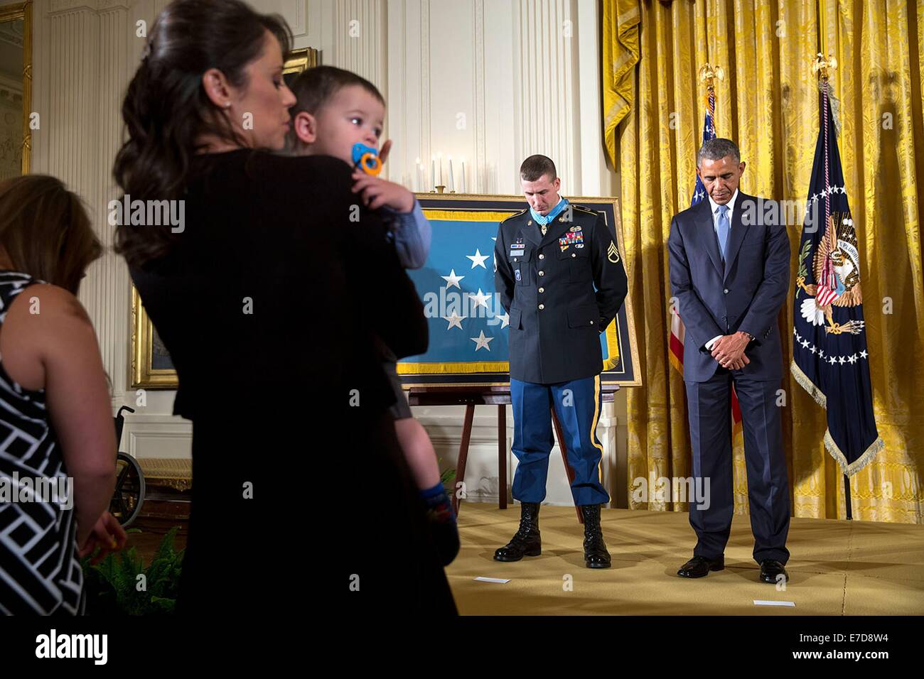 US President Barack Obama and Staff Sergeant Ryan M. Pitts bow their heads during the benediction following the Medal of Honor ceremony for SSG Pitts in the East Room of the White House July 21, 2014 in Washington, DC.  At left is SSG Pitt's wife Amy and one-year-old son Lucas. Stock Photo