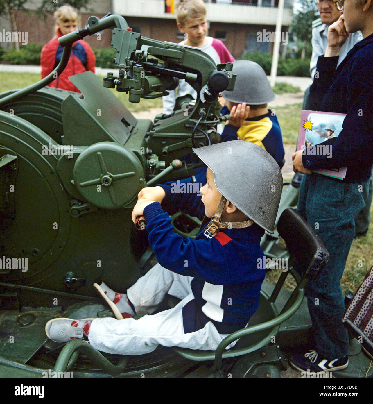 Children wearing steel helmets sit at a canon, which the National People's Army showed to the public during the 22nd Workers' Festival in Frankfurt Oder, East Germany, 24 June 1988. During the public events and festivities, the NPA was present to demonstrate their close relationship to the people. Photo: Hans Wiedl Stock Photo