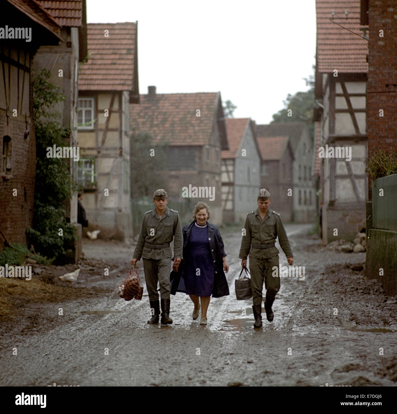 Two border soldiers from the East German National People's Army carry border unit cook Berta Niebel's bags and shopping nets through the derelict town Motzlar in der Rhoen, Germany, October 1968. The town is located directly in the border region between East and West Germany. It was empty and a special permit was needed to visit the town. Photo: Wilfried Glienke Stock Photo