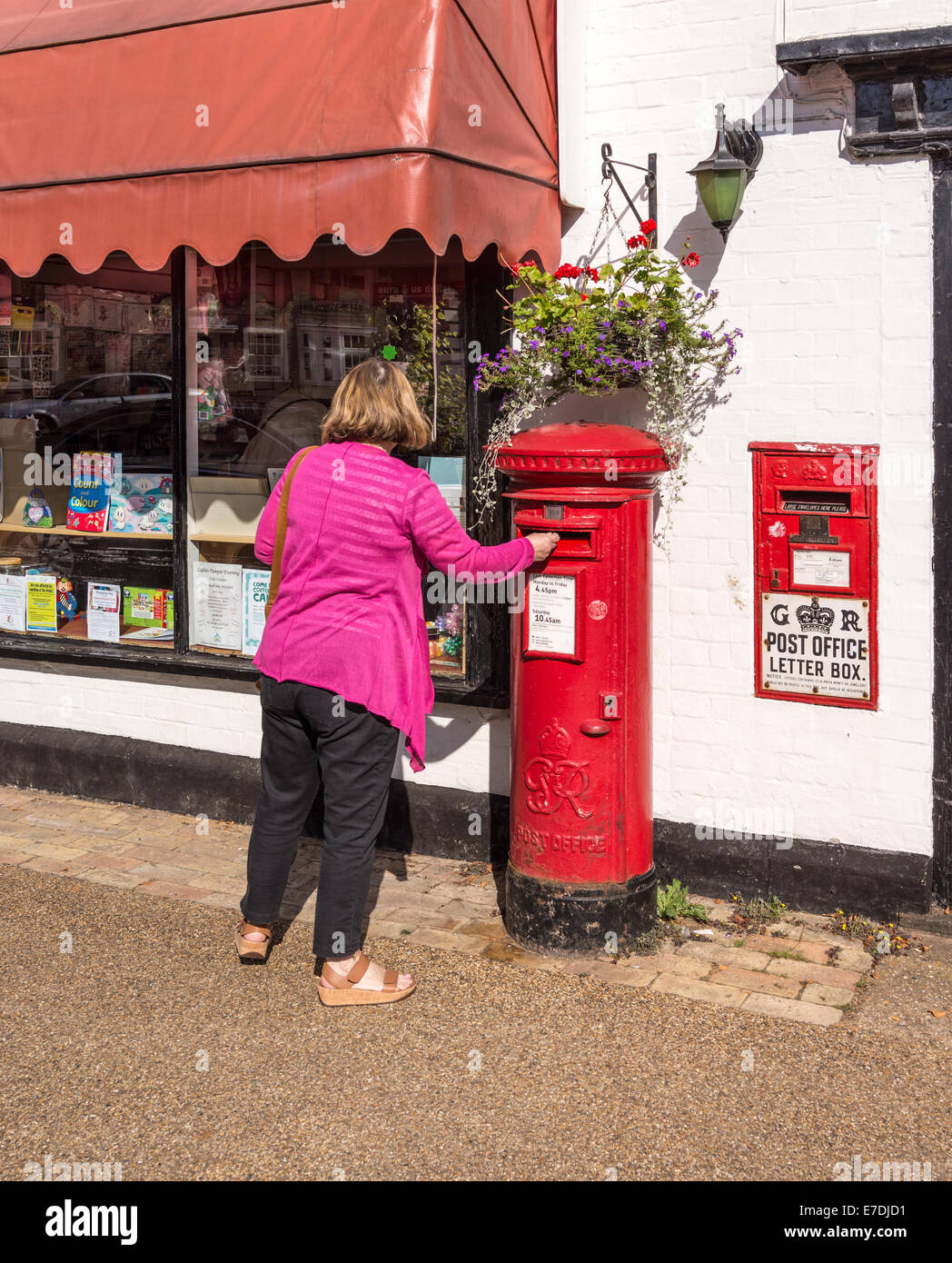 Woman posting a letter in an old fashioned post box in Woolpit Suffolk