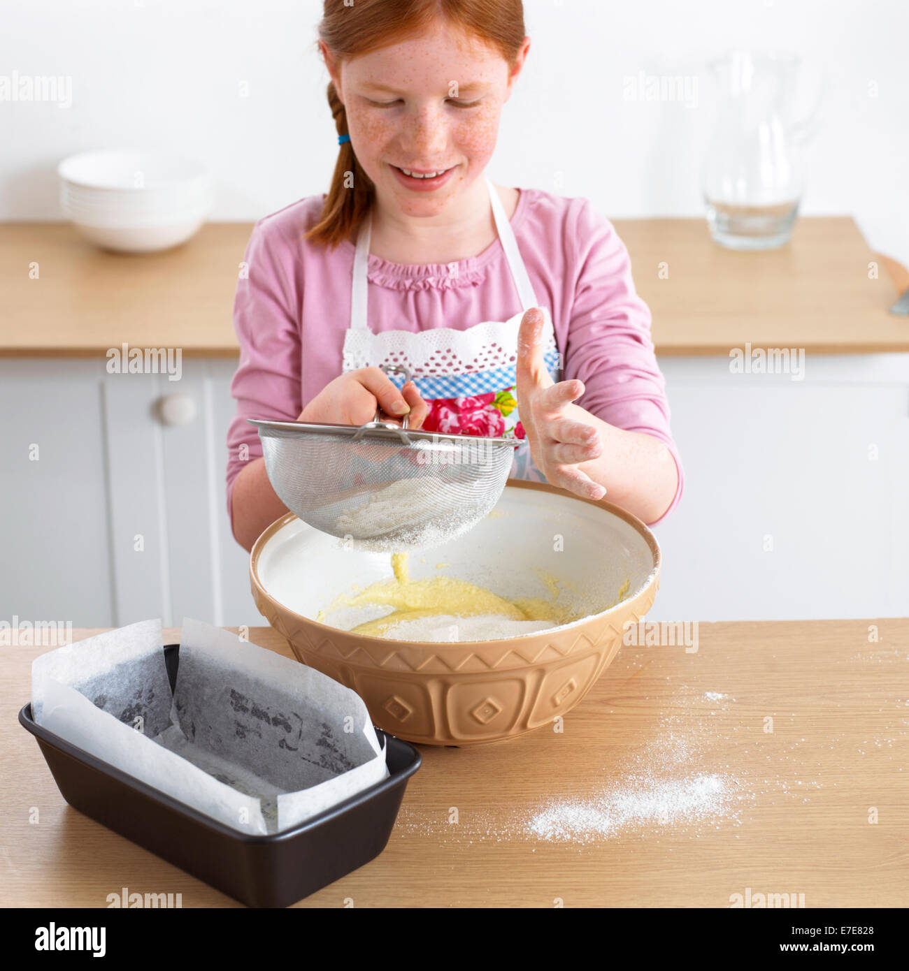 red haired girl sifting flour into mixing bowl 8-9 years Stock Photo