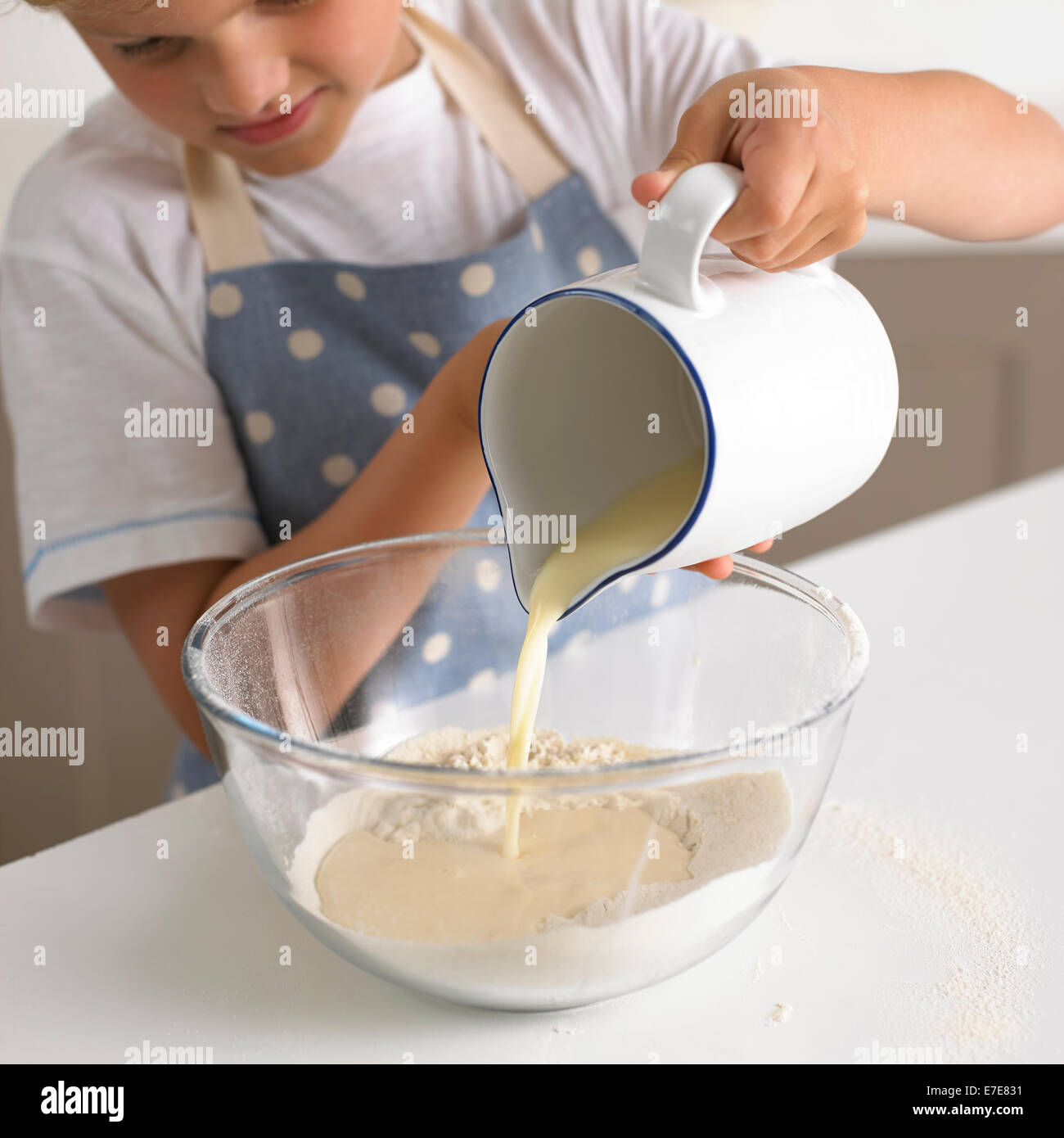 young boy 6-7 years pouring milk into flour to make batter for pancakes Stock Photo