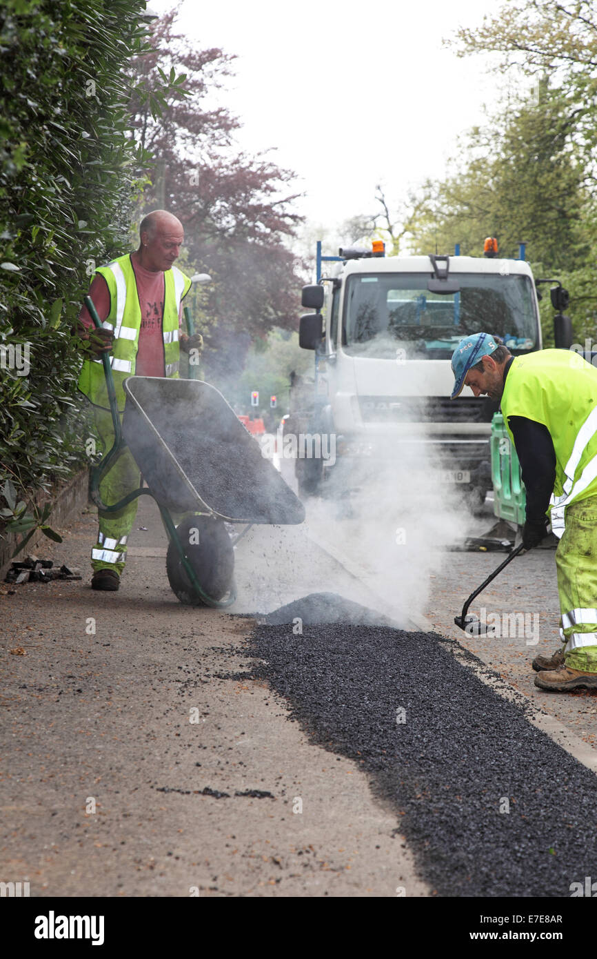 Workmen lay asphalt to a footpath after the installation of new fibre-optic cables for high speed broadband Stock Photo