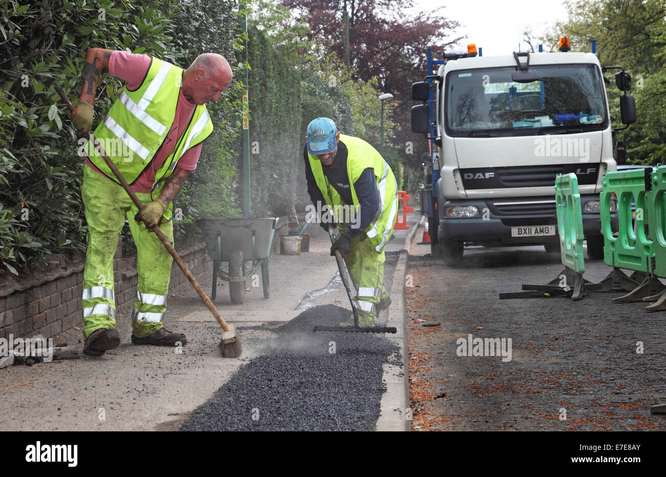Workmen lay asphalt to a footpath after the installation of new fibre-optic cables for high speed broadband Stock Photo