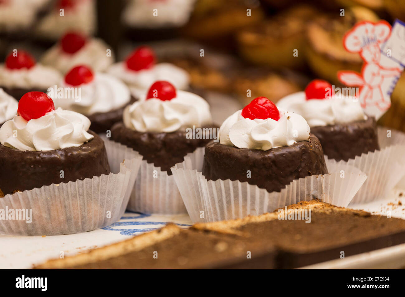 Chocolate pastries with whipped cream and candied cherry on a tray for sell in a traditional Mexican bakery (pasteleria). Stock Photo