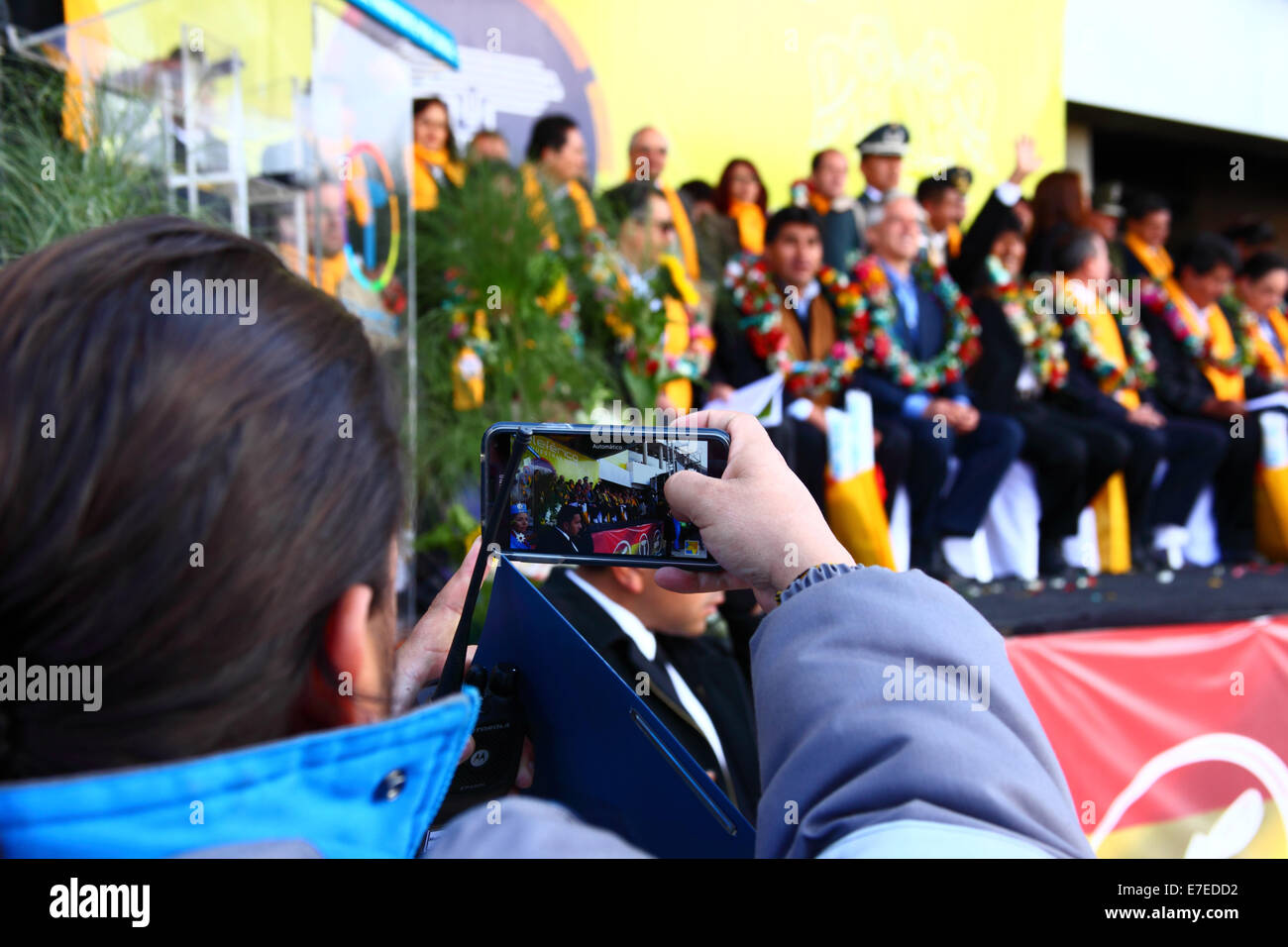 El Alto, Bolivia, 15th September 2014. A Mi Teleferico company worker films the inauguration ceremony of the Yellow Line on his smartphone at the station in Ciudad Satelite. Credit:  James Brunker / Alamy Live News Stock Photo