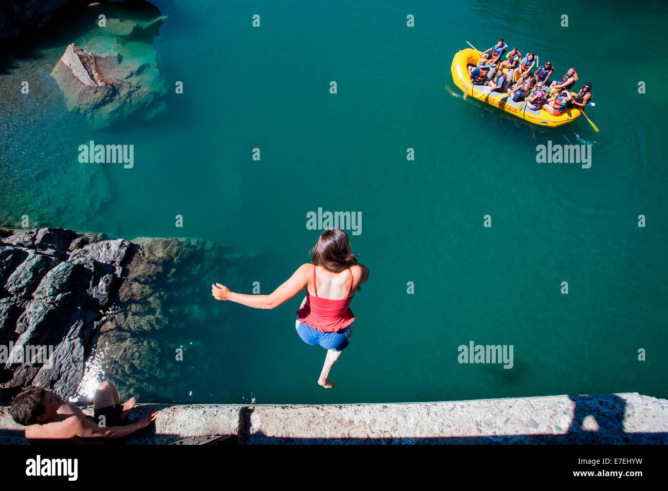 A girl jumps from a high bridge into a river of clear, blue-green water ...