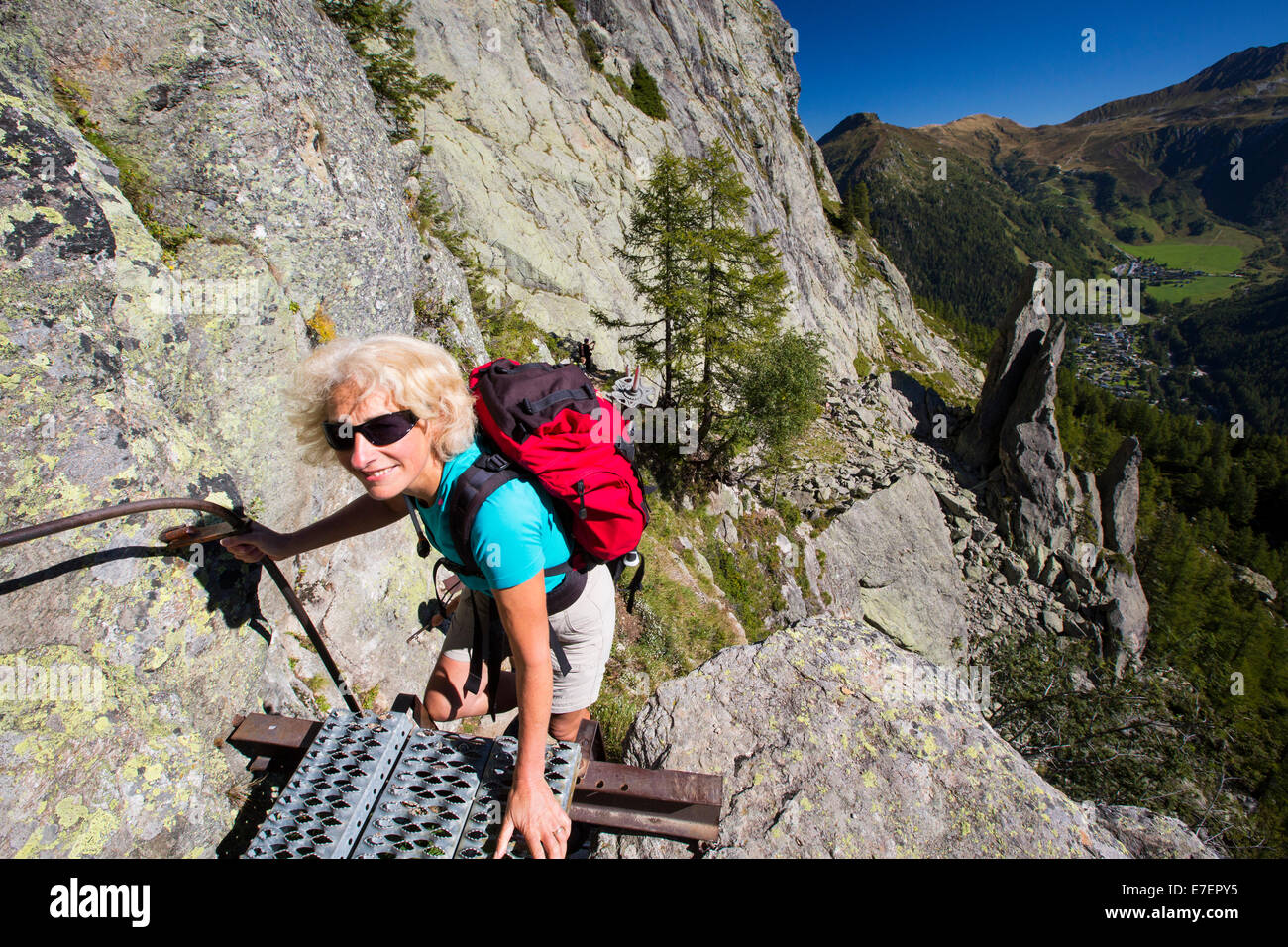 A woman climbing ladders in the Aiguille Rouge range above, Chamonix