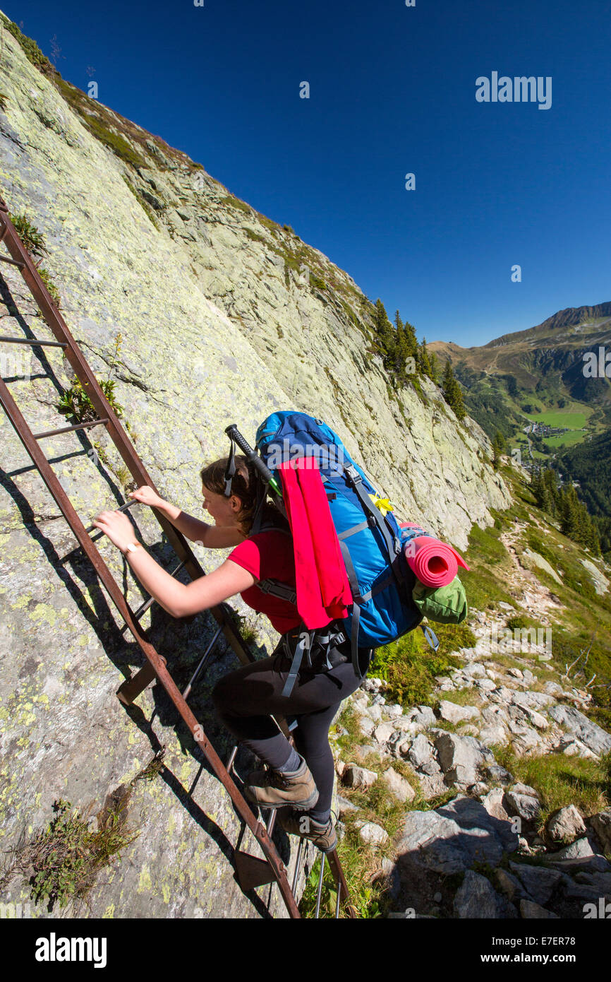 A woman climbing ladders in the Aiguille Rouge range above, Chamonix