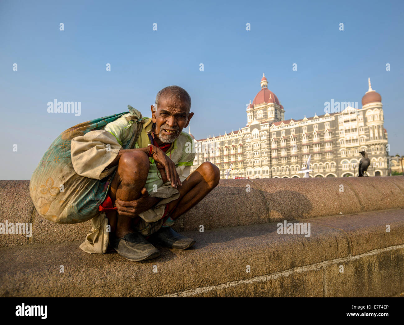 A beggar is sitting in front of the luxurios Taj Mahal Palace Hotel in the suburb Colaba, Mumbai, Maharashtra, India Stock Photo