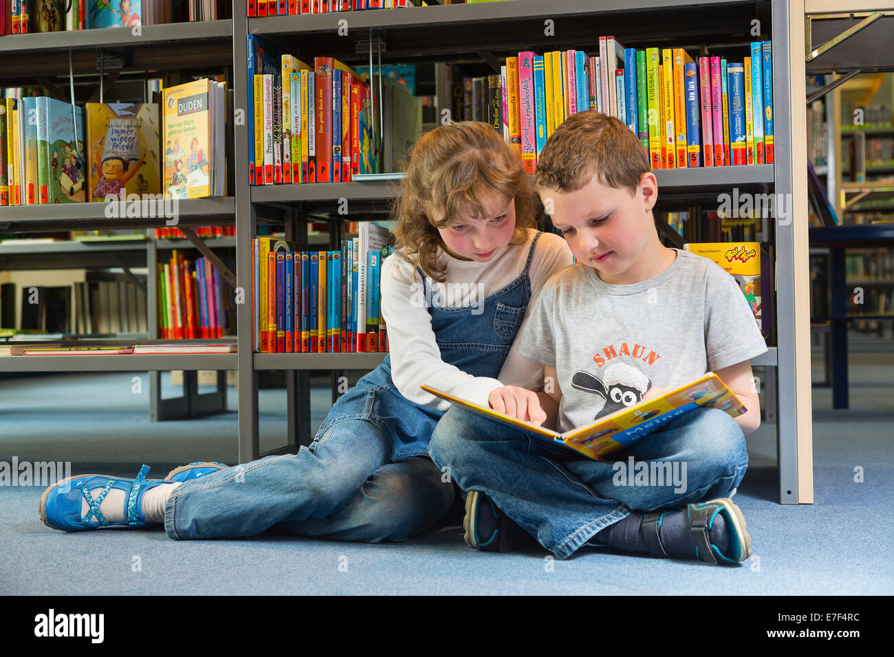 Two children reading reading a book in a public library, Coswig, Saxony, Germany Stock Photo