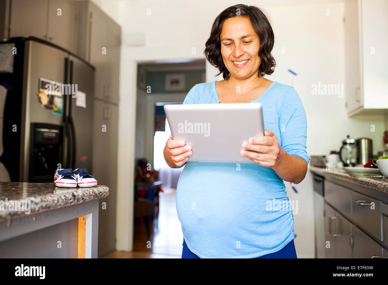 Pregnant Hispanic woman using tablet computer in kitchen Stock Photo