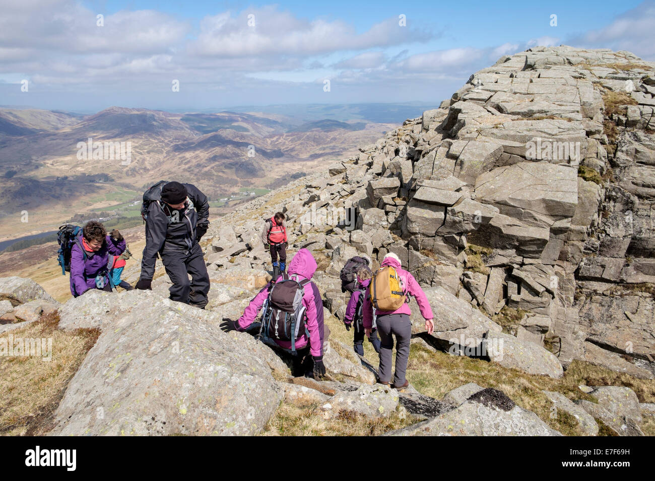Hikers scrambling over rocks on Carnedd Moel Siabod top ridge in mountains of Snowdonia National Park (Eryri) above Capel Curig, North Wales, UK Stock Photo