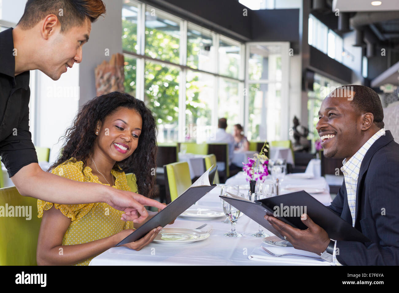 Waiter explaining menu to couple in restaurant Stock Photo