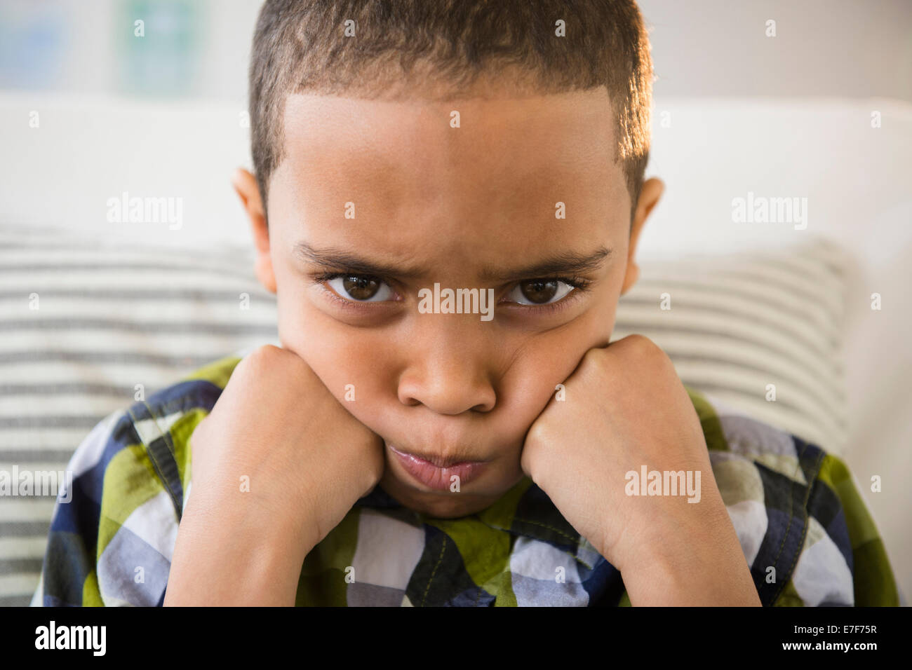 Mixed race boy pouting on sofa Stock Photo